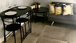 Una sala de estar moderna con un sofá, dos mesas de comedor y sillas. Hay un televisor de pantalla plana en la pared, un cuadro abstracto enmarcado y una ventana con cortina oscura.