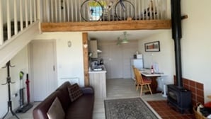Ett rum i loftstil med ett träpanelat tak, en brun lädersoffa, ett matbord med stolar, en köksdel och en öppen spis.