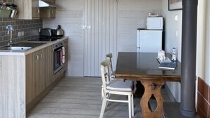 Ett kompakt kök med träskåp, en inbyggd ugn, ett matbord med stolar, en svart spis och en surfbräda som hänger i taket.