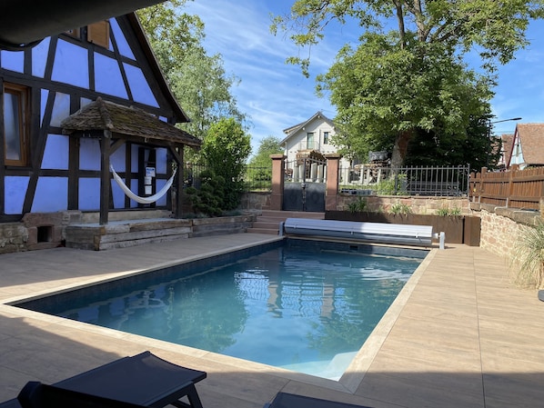 Una piscina con cubierta de madera, una hamaca y un edificio tradicional con entramado de madera.