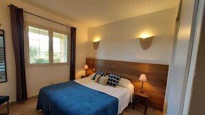 A bedroom with a large bed, two bedside tables, a window with curtains, and wall-mounted lighting. - Beautiful apartment in Residence with swimming pool, garden and terrace (Sainte-Lucie de Porto-Vecchio)