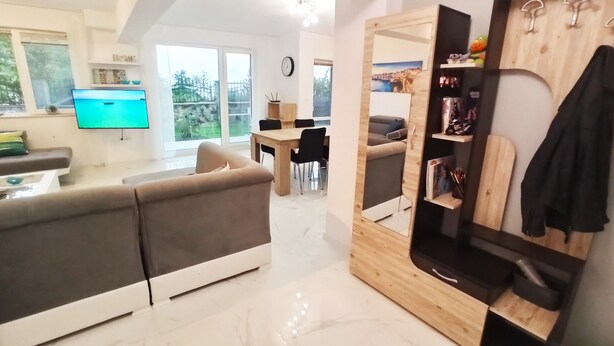 A modern living room with a sofa, a dining table, and a TV. There is a wooden cabinet with a mirror and shelves. - Fabulous holiday home with sea view for the whole family! (Balchik)