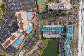 Vista aérea de un hotel con múltiples piscinas, un estacionamiento amplio y una zona de playa con sombrillas.