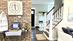 Un salon chaleureux avec un mur en briques, un escalier en bois et un canapé blanc.