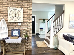 Un salon chaleureux avec un mur en briques, un escalier en bois et un canapé blanc.