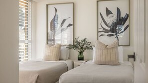 Un dormitorio con dos camas, una mesita de noche, un jarrón con flores y cuadros en la pared.