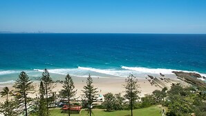 A coastal view with a beach, clear blue sea, and a distant city skyline. - Orion 6 - Beachfront Rainbow Bay - All Linen Supplied - Min. 3 Night Stays! (Rainbow Bay)