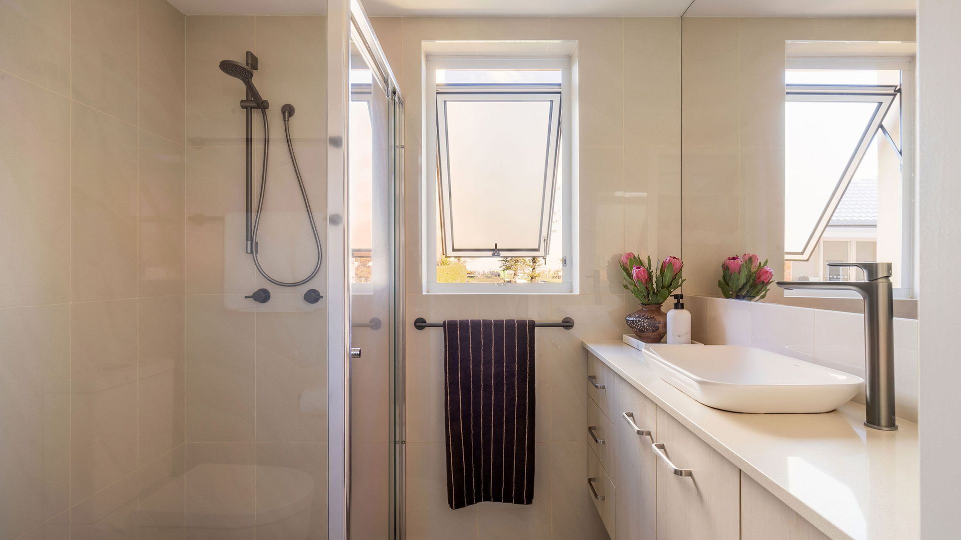 A modern bathroom with a shower, a window, a sink, and a towel rack.