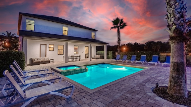 A modern two-story house with a swimming pool, outdoor seating, and a sunset sky. - Grand Traverse Paradise | 8-Bedroom Villa w/ Private Pool at Reunion Resort (Kissimmee)