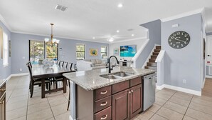 A modern kitchen with a central island, a dining area with a large table, and a staircase leading to another level. - Grand Traverse Paradise | 8-Bedroom Villa w/ Private Pool at Reunion Resort (Kissimmee)