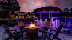 An outdoor patio with a fire pit, lounge chairs, and a thatched-roof structure. - Grand Traverse Paradise | 8-Bedroom Villa w/ Private Pool at Reunion Resort (Kissimmee)
