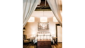 Une chambre à coucher avec un lit en métal, deux tables de chevet avec des lampes, un plancher en bois et une grande fenêtre avec des rideaux.