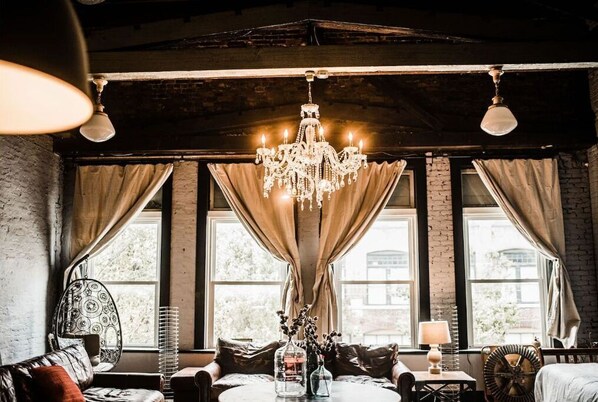 Relax in a charming room with a comfortable seating area, sofa, and round table, featuring a large chandelier and large windows.