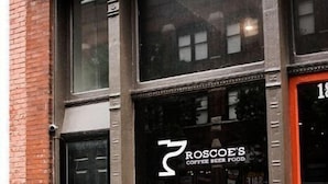 Un bâtiment avec une enseigne indiquant « ROSCOE'S : CAFÉ, BIÈRE, RESTAURATION » et une grande fenêtre.