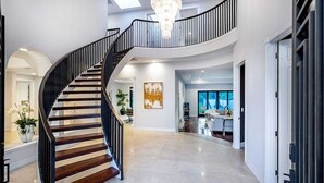 A spacious, modern interior with a curved staircase, a chandelier, and a large window. - The Light of Mount Olympus (Los Angeles)