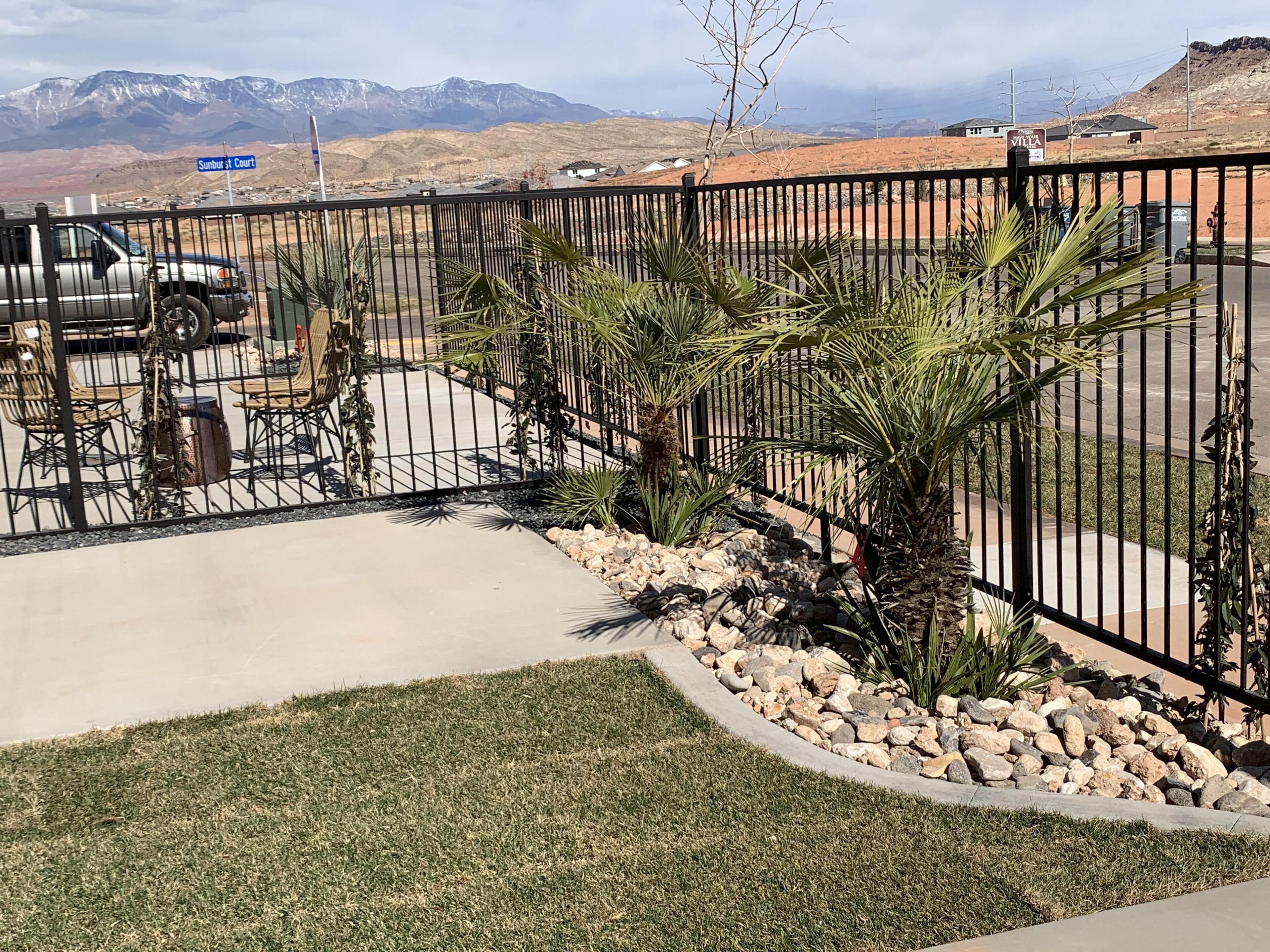 A fenced outdoor area with a concrete patio, palm trees, and a view of mountains in the background.