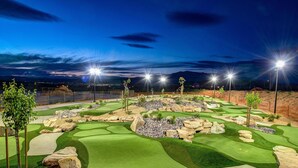 Un campo de golf de noche con zonas bien iluminadas, fairways verdes y búnkeres.