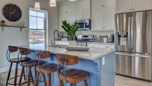 Una cocina moderna con armarios blancos, electrodomésticos de acero inoxidable y taburetes de madera.