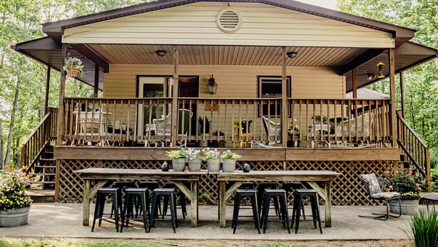 Een houten chalet met een overdekt terras, buitenmeubels en plantenpotten.
