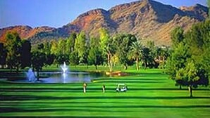 En golfbana med en damm, träd och berg i bakgrunden.
