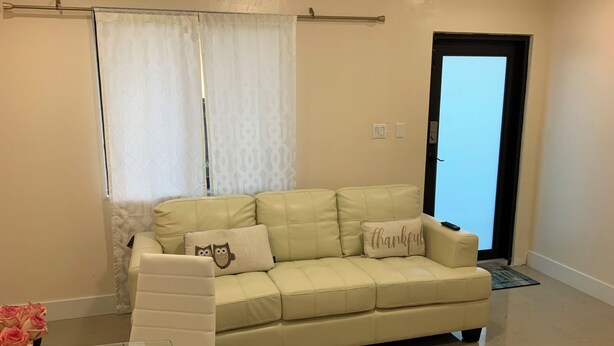 A beige leather sofa with two cushions, one with an owl design and another with the word "thankful". A clear glass table is in front of the sofa, and a vase of pink roses is on the left. - Everything is pretty much walking distance which is odd for Miami  (Hialeah)