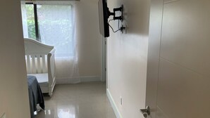 A room with a white crib, a window with a sheer curtain, and a wall-mounted TV. - Everything is pretty much walking distance which is odd for Miami  (Hialeah)