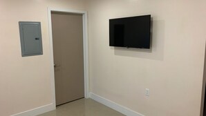A hallway with a door, a wall-mounted electrical box, and a TV. - Everything is pretty much walking distance which is odd for Miami  (Hialeah)