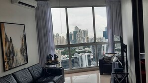 A modern living room with a large window, a black leather sofa, a small table with decorative items, and a framed abstract painting on the wall. - Panama from the sky in the Financial  District (Panamá)