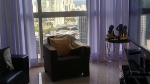 A spacious living room with a large window, a black sofa, a small table with decorative items, and a flat-screen TV. - Panama from the sky in the Financial  District (Panamá)