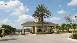 A gated entrance to a building with a covered patio area, palm trees, and a clear sky. - Windsor Wonderland!  Your Disney Getaway! Water slides, pool, arcade and more! (Kissimmee)
