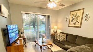 A living room with a grey sofa, a wooden coffee table, a TV on a wooden stand, and a ceiling fan. - Windsor Wonderland!  Your Disney Getaway! Water slides, pool, arcade and more! (Kissimmee)
