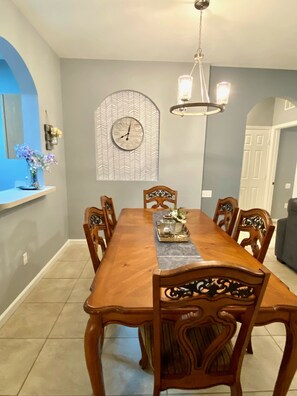 Une salle à manger avec une table en bois, des chaises, un lustre, une horloge et un élément décoratif mural.