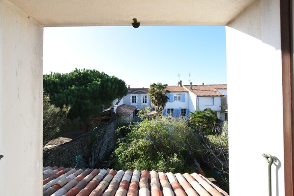 A view from a balcony overlooking a residential area with terracotta-tiled roofs, a stone wall, and greenery. - Maison Rose, La Couarde s/ mer, rénovée, en plein coeur de l île de ré ! (La Couarde-sur-Mer)