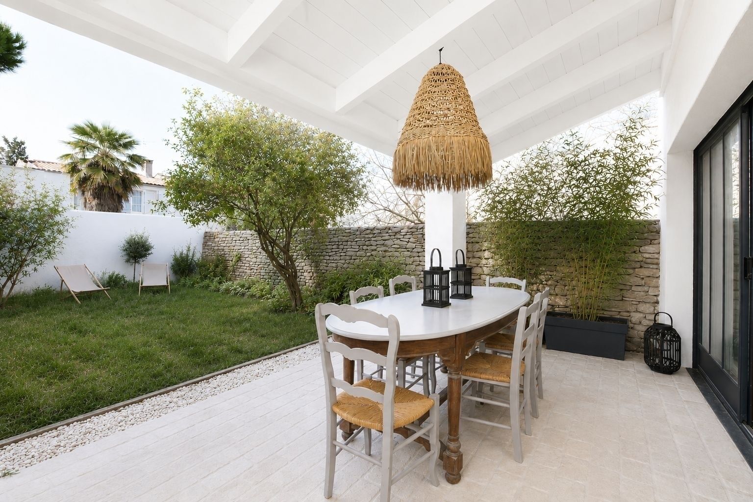 An outdoor patio with a round table, white chairs, and a woven hanging light fixture.