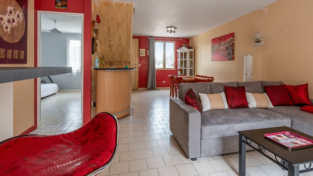 A modern living room with a grey sofa, red chair, and a wooden bar area. - Villa Bagatelle, et son jardin - Welkeys (Montpellier)