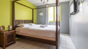 A four-poster bed with white linens, a wooden nightstand with a lamp, and a mirror on the wall. - Villa Bagatelle, et son jardin - Welkeys (Montpellier)