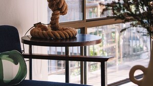 Une table ronde avec une lampe suspendue à une corde, un canapé bleu et une vue sur l’extérieur par une fenêtre.