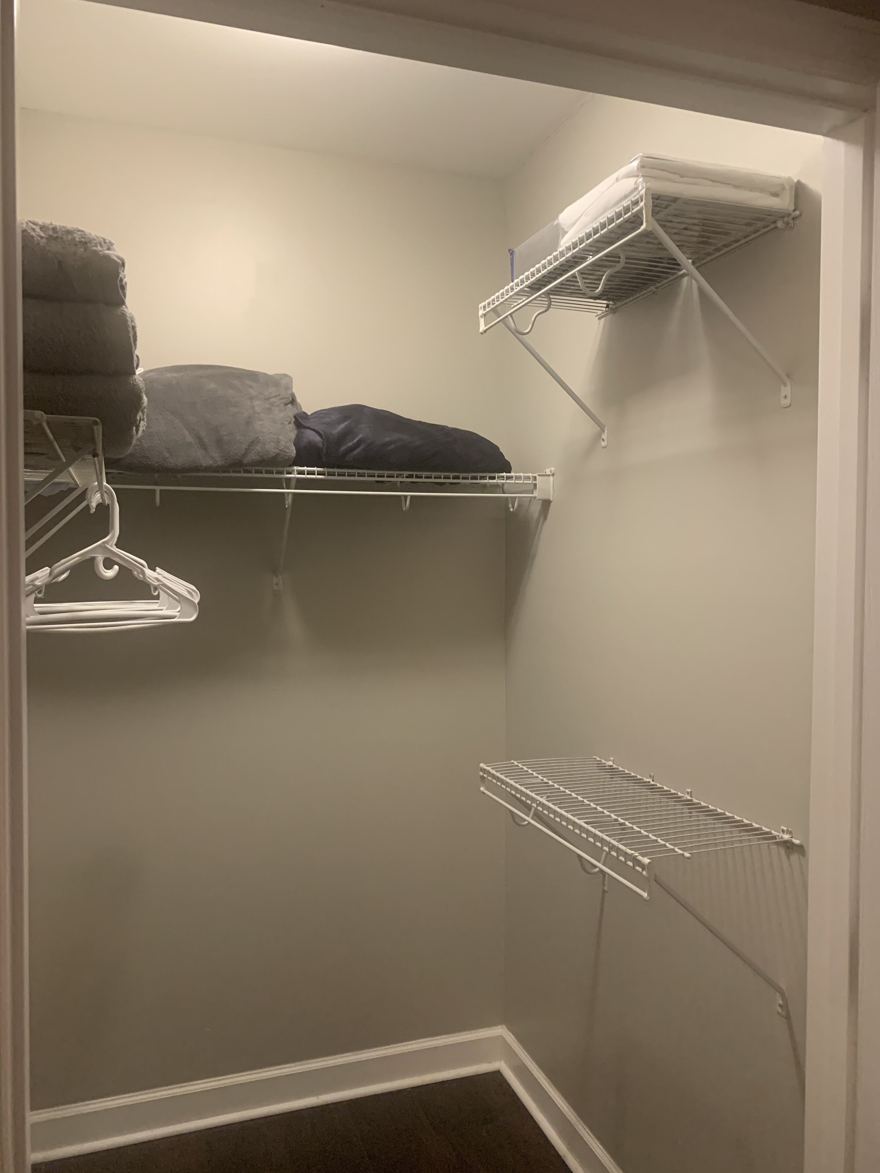 A walk-in closet with white metal shelves and a metal drying rack.