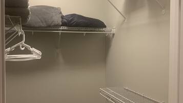 A walk-in closet with white metal shelves and a metal drying rack.