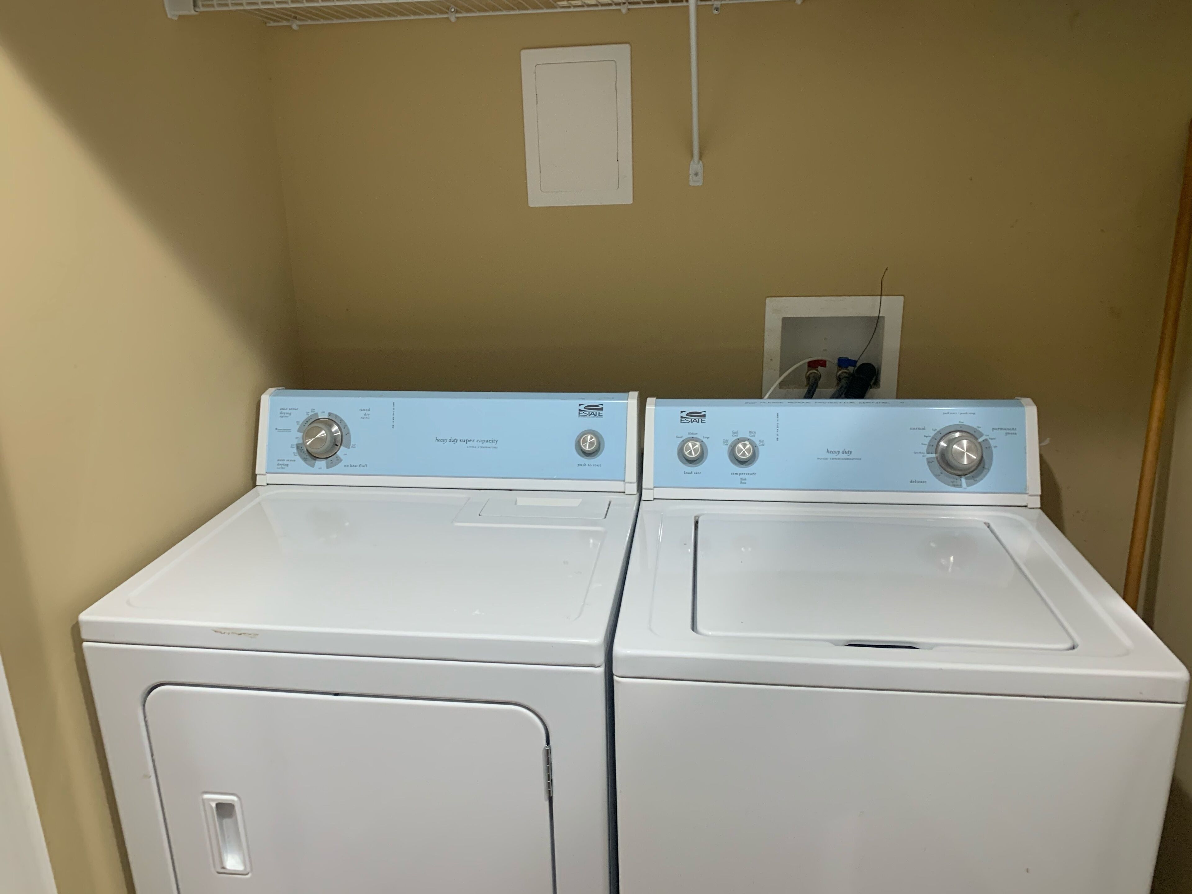 Two white front-loading washers with control panels, a beige wall, and a white door.