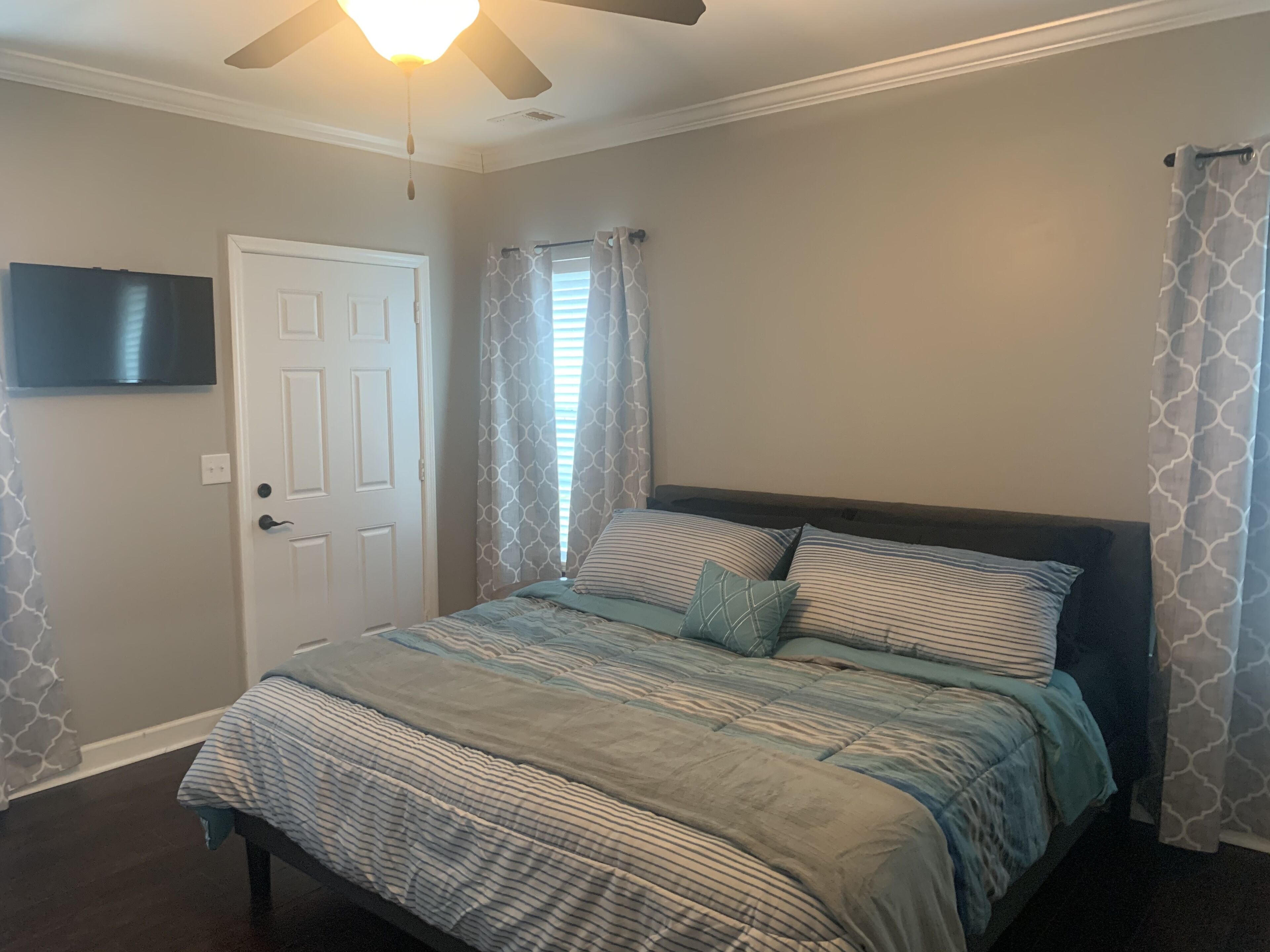 A bedroom with a bed, a ceiling fan, a door, and a window with curtains.