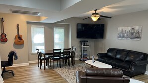 A living room with a dining area, a black leather sofa, a TV mounted on the wall, and a ceiling fan. - Newly remodeled, Hot Tub, 70n inch tv Private Entrance, Convenient location (Lebanon)