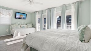 Ein Schlafzimmer mit einem großen Bett, einem kleineren Bett, einem Deckenventilator und einem Fenster mit Vorhängen.