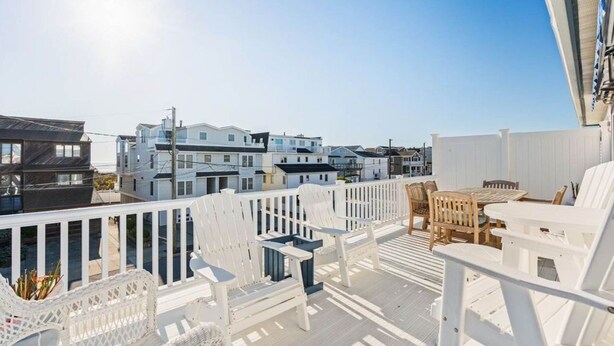 Eine Terrasse mit weißen Geländern, Korbstühlen und einem Holztisch.