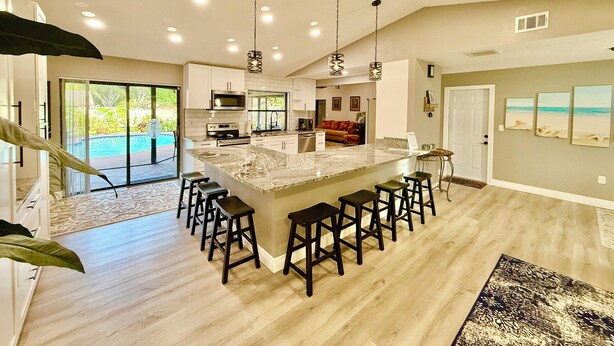 A spacious kitchen with a large island, bar stools, and a view of a pool. - SPACIOUS home, private POOL,5 mins to beach! Walk to Publix. Great for families! (Seminole)