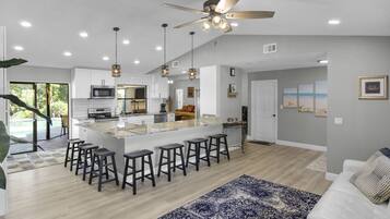 A modern kitchen with a central island, bar stools, and a ceiling fan.