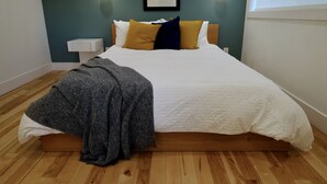 A neatly made bed with a white and gray blanket, a wooden headboard, and two bedside tables with wall-mounted lights.