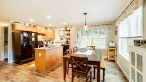 A spacious kitchen with wooden cabinets, a central island, and a dining area with chairs and a table. - 'Greystone' Creekside Cabin: Hike, Fish & Explore! (Elk Park)