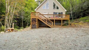 A cabin with a wooden deck, a staircase, and a log pile. - 'Greystone' Creekside Cabin: Hike, Fish & Explore! (Elk Park)