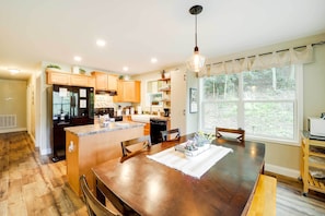 A modern kitchen with wooden cabinets, a central island, and a dining area with a large table. - 'Greystone' Creekside Cabin: Hike, Fish & Explore! (Elk Park)